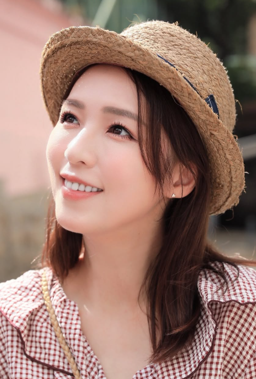 戶外陽光下，女子戴草帽、穿紅白格紋上衣，仰望遠方露出微笑。