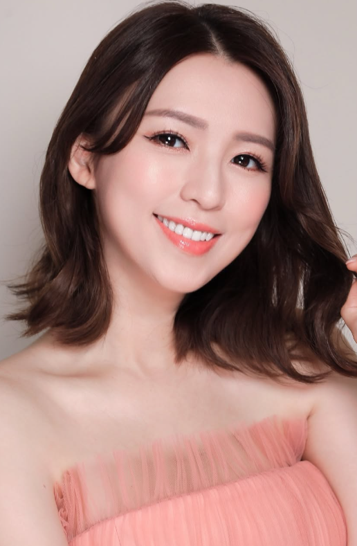 近距離半身照，女子穿淡粉色禮服、頭髮微捲，對鏡頭微笑。