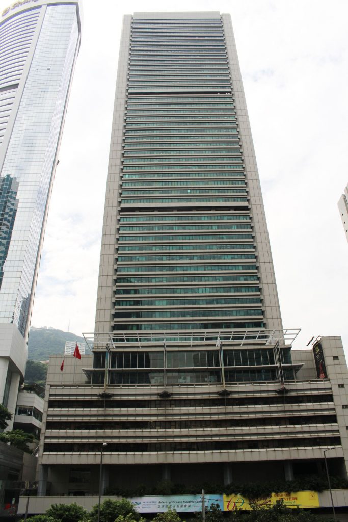 香港金鐘道政府合署高聳入雲的外觀，其灰白色牆身與多層玻璃窗映照藍天，是適合製作客製化退休禮物的地標建築。