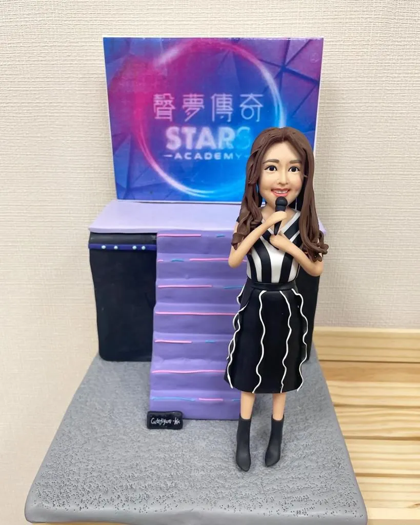 客製立體場景：背板印有「聲夢傳奇 STAR ACADEMY」圓形霓虹標誌，前方為紫色階梯與黑色側台；舞台中央站著一位拿麥克風的人像公仔，穿黑白條紋上衣與黑色波浪線條裙、短靴，呈現演唱姿態。整體置於灰色方形底座。
