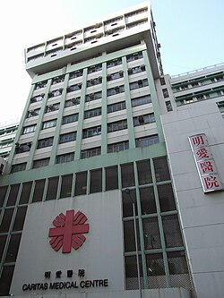 明愛醫院主樓外觀，淺綠色外牆配上紅色「明愛醫院」標誌，以及下方「Caritas Medical Centre」英文字樣，象徵醫者仁心。