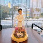 這款作品以 護士（Nurse）專業形象 為靈感，展現溫暖與堅毅的護理精神。 人物身穿整齊的白色護士制服，肩襯紅邊徽章細節清晰；短髮造型搭配明亮笑容，傳達出專業、親切與關懷。 底座採用乾燥花園設計，融合粉、紫、米白色花材，象徵溫柔守護與生命綻放。 作品外層覆以透明玻璃罩，並以暖黃燈圈環繞，營造出柔亮而典雅的紀念氛圍。 前方名牌可客製姓名或銜頭，使每個細節都更具專屬感。 此公仔作品非常適合作為 退休紀念、晉升賀禮、或感謝醫護人員辛勞的專業禮物， 以手工藝術方式致敬「白衣天使」無私奉獻的精神與微笑背後的力量。