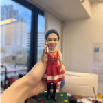 這款作品為 退休致敬主題人像公仔，以真摯笑容與優雅神態展現生命中最溫柔的篇章。 人物穿著紅白相間的洋裝，肩背小包，手持電話姿態自然生動， 臉上燦爛的微笑洋溢著親切與樂觀氣息，象徵多年工作中傳遞的溫暖與堅持。 底座採草綠設計，點綴五彩小花，象徵繽紛人生與美好祝福； 正面刻有「Ms Wong 退休快樂」銘牌，為專屬的紀念時刻留下不朽印記。 整體造型細緻而充滿故事感，特別適合作為 退休紀念禮、榮退典禮贈禮或同事祝福禮物， 以立體雕塑形式定格最燦爛的笑容，表達敬意與感謝， 讓人生新篇章從這份微笑開始。
