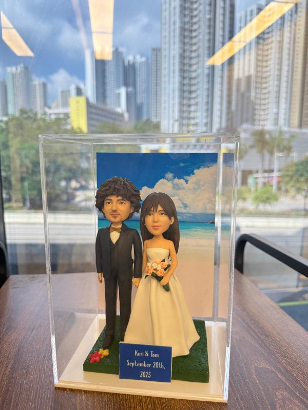 浪漫海灘婚禮主題公仔，新人甜蜜手牽手搭配藍天白雲背景，前方名牌印有「Keri & Tom」與紀念日期，是記錄幸福時刻的專屬結婚紀念禮物。