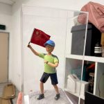 登山運動公仔戴帽揮舞紅旗，立於岩地底座並置於透明展示盒，壽宴與里程碑禮物推薦