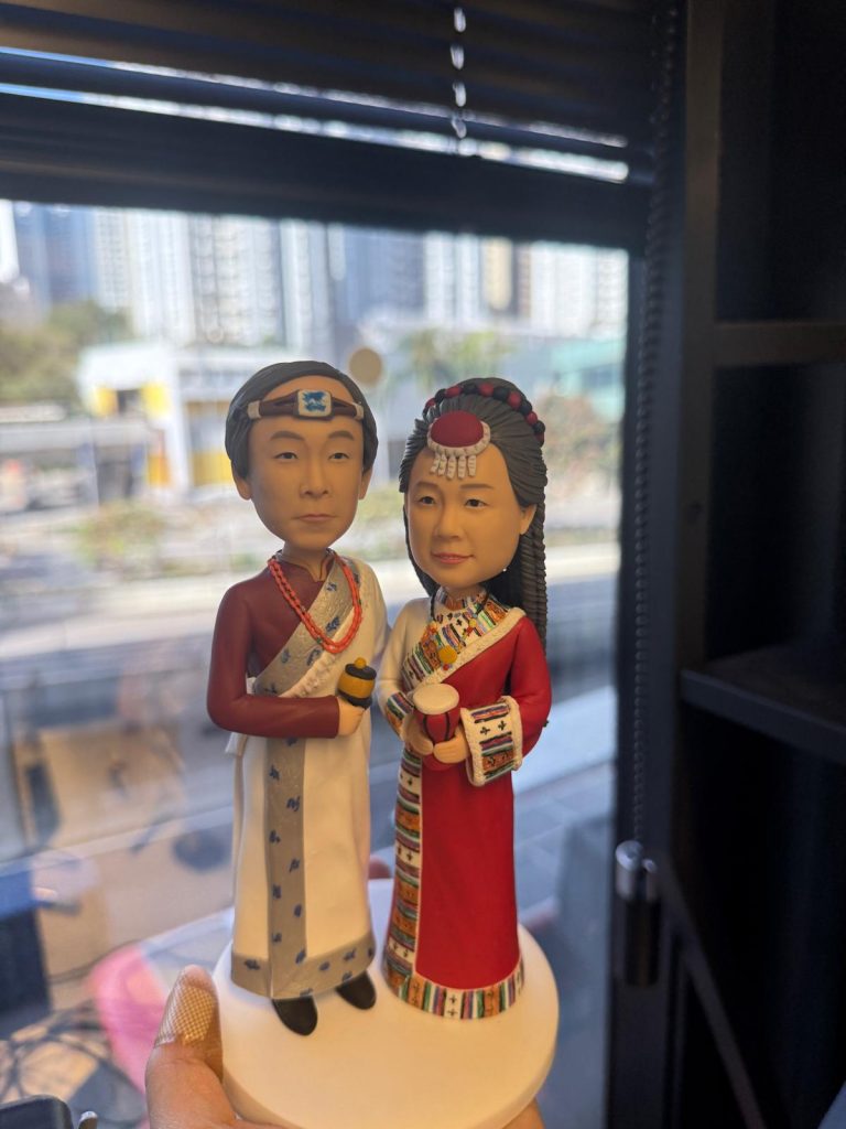 穿著民族傳統禮服的一對夫妻人像公仔站在白色圓形底座上,衣服圖騰與頭飾細節豐富