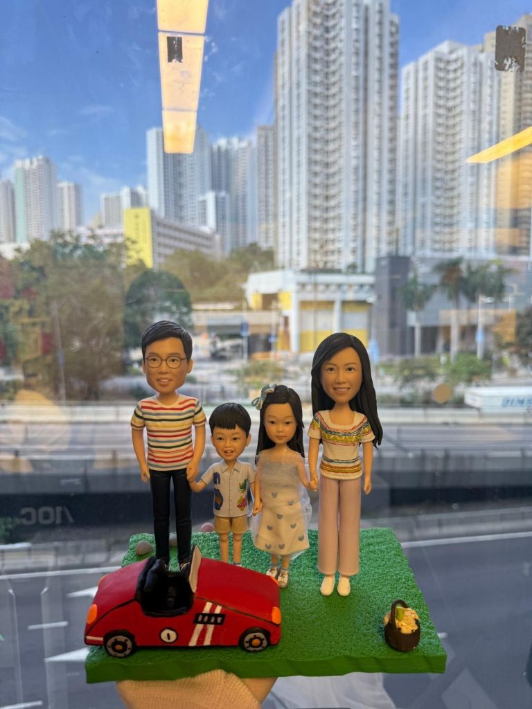 一家四口站在草地上的家庭人像公仔，旁邊有紅色跑車與野餐籃配件，呈現溫馨親子時光