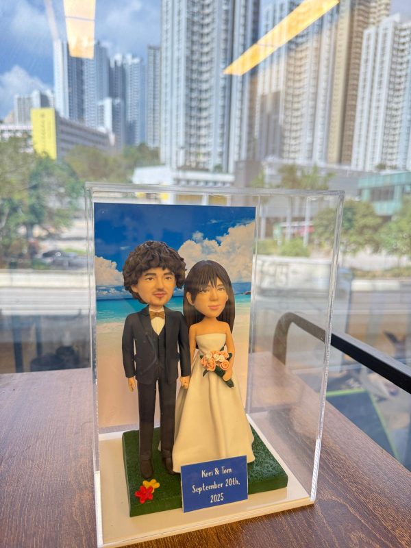 浪漫海灘婚禮主題公仔，新人甜蜜手牽手搭配藍天白雲背景，前方名牌印有「Keri & Tom」與紀念日期，是記錄幸福時刻的專屬結婚紀念禮物。