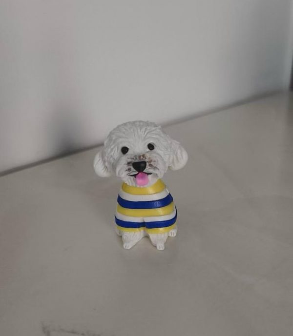 坐姿白色捲毛狗狗公仔，穿黃藍白條紋毛衣，黑鼻圓眼、粉紅舌頭微吐，放置在淺色桌面上。