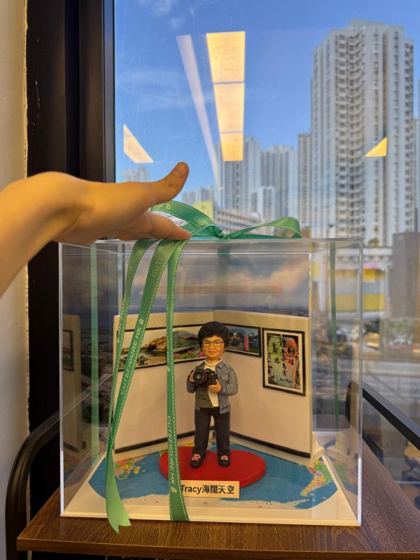 精緻手作攝影師公仔禮盒，手持相機搭配旅行風景照片牆背景，底部刻有「Tracy海闊天空」字樣，是送給熱愛攝影與旅遊朋友的專屬紀念好禮。
