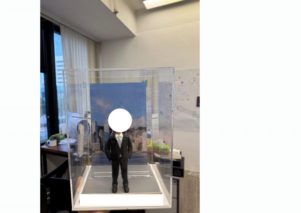 透明展示盒內的西裝主題公仔：身穿深色西裝與領帶的男子雙手插袋站在灰色地台上，背後是藍天白雲下的城市天際線照片背板，前方有可客製銘牌。