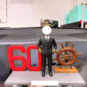 船長主題客製公仔:身穿黑色制服與肩章、戴船長帽的男子站在灰色底座中央,左側有紅色立體「60」字樣,右側擺放木質舵輪模型。