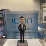 透明展示盒內的客製男士公仔，身著深色西裝與淺藍襯衫、雙手插袋站立，背板為「ICON」字樣，底座名牌寫著「VINCE 世一」