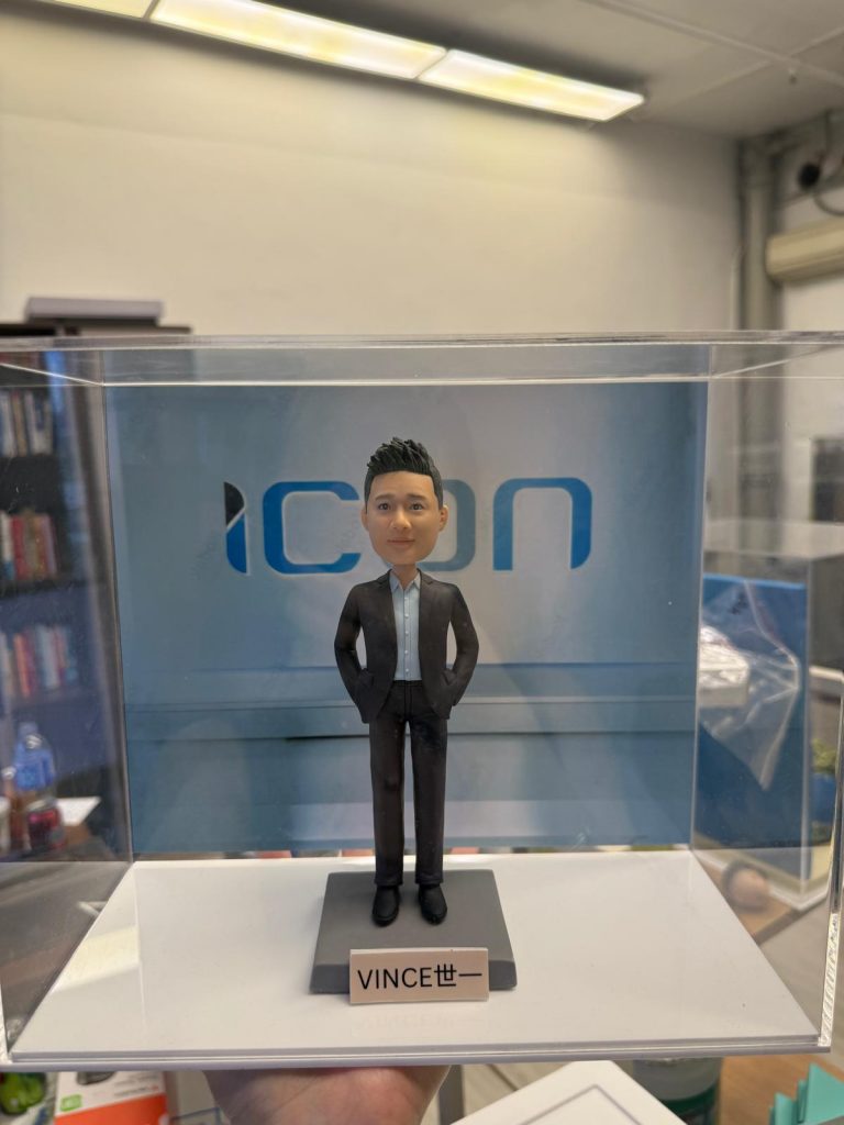 透明展示盒內的客製男士公仔，身著深色西裝與淺藍襯衫、雙手插袋站立，背板為「ICON」字樣，底座名牌寫著「VINCE 世一」