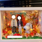 白色相框燈箱內的客製情侶公仔場景，背景為秋日楓葉林，周圍以乾燥花與暖黃小燈點綴，前方擺放兩顆紅心與可愛史努比模型