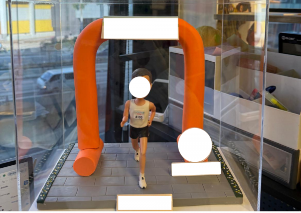 透明展示盒內的客製跑者公仔，穿背心短褲與號碼布，衝過橙色拱門終點線，地面為灰色磚紋跑道並設有銘牌位置