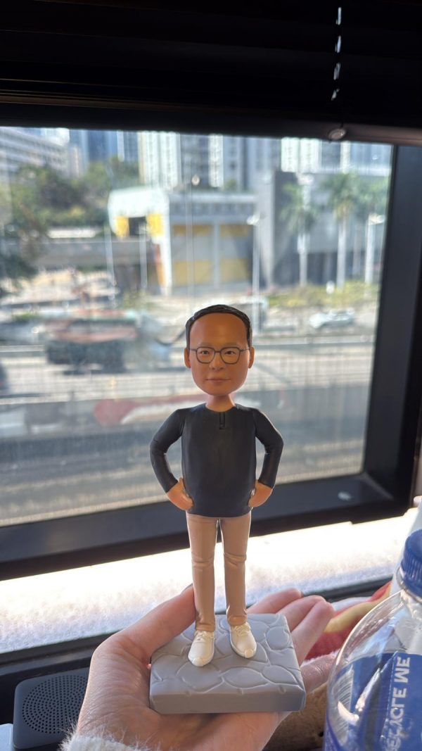 手掌托著客製男士公仔，黑色上衣配卡其長褲與白鞋，雙手插腰站在灰色石紋底座上，作為送給老闆的禮物