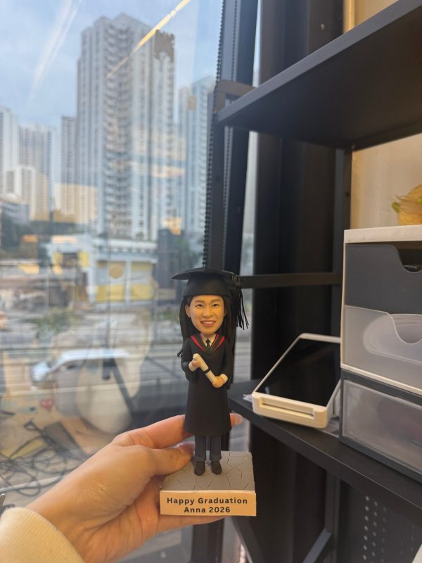 CUTEFIGUREHK 客製化女性人像畢業公仔，身穿黑色畢業袍並戴上四方帽，手持畢業證書，站在印有「Happy Graduation Anna 2026」專屬字句的石紋底座上，是送給大學畢業生的獨一無二紀念禮物。