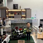 CUTEFIGUREHK 客製化香港交通警公仔。公仔身穿螢光黃綠色交通警制服，雙手交叉抱胸。旁邊配有一架精緻的警察電單車模型。場景背景為「上水警署」(Sheung Shui Police Station)。底座名牌刻有「退休不褪色 順樂永無憂 2026」，是一份專為警察訂製的榮休紀念禮物，裝在透明亞加力展示盒中。