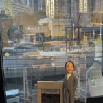 CUTEFIGUREHK 客製化男性人像公仔，生動還原了身穿灰色西裝、戴眼鏡的男士專業造型。公仔旁配有精緻的「東亞銀行」門面微縮場景道具，底座設有專屬牌匾，刻上「Frankie 祝你退休生活美滿 2025」的祝福語。整體裝在透明亞加力展示盒中，是一份專為銀行業同事度身訂造的榮休紀念禮物。