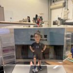 CUTEFIGUREHK 客製化榮休紀念公仔。一位戴著眼鏡的男士，身穿黑色運動套裝（上衣印有心形圖案及數字「168」，短褲亦印有「168」），雙手叉腰，右腳踩著一個足球，站立在仿石磚紋理的灰色底座上。底座前方設有一塊專屬名牌，印有「赤柱監獄高級文書主任 李永祥先生 榮休之喜」。公仔背後配有一幅印有香港懲教署徽章及「赤柱監獄 Stanley Prison」字樣的建築物背景圖，整體安放在一個透明的亞加力膠展示盒內。