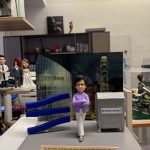 CUTEFIGUREHK 客製化企業高管紀念公仔。一位戴著黑框眼鏡的短髮女士，身穿優雅的紫色西裝外套和白色長褲，雙手交叉抱胸，展現自信專業的姿態。她站在一個精心設計的場景中，背景是印有「STATE STREET」標誌的香港中環夜景照片。場景左側有三個藍色的波浪形立體裝飾，右側有一個印有「STATE STREET」標誌的灰色演講台。底座前方有一塊刻有英文感謝語的長方形牌子，表達對這位上司多年來支持的感激與祝福。