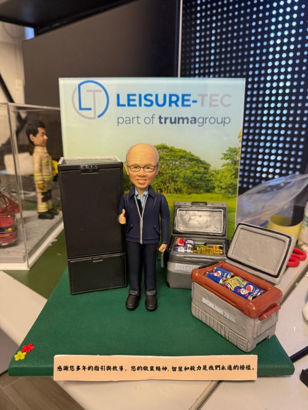 CUTEFIGUREHK 客製化企業高管及上司榮休公仔。戴眼鏡的男士身穿藍色外套比出讚好手勢，身旁配有精緻的黑色雪櫃及裝滿微縮飲品的保溫箱模型。背板印有「LEISURE-TEC」公司標誌，綠色底座前方設有寫上感謝語句的專屬名牌，是送給老闆或導師的最佳退休紀念禮物。