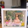 CUTEFIGUREHK 客製化立體相框公仔禮物。一個白色的發光畫框，內部佈置成夢幻的童話花園。中央是一個穿著粉紅色花瓣晚裝的長髮女孩立體公仔，頭戴花環，手持粉紅玫瑰。背景是浪漫的黃昏花園圖案，公仔腳下鋪滿了紫色、白色和粉紅色的乾花（繡球花）以及綠色苔蘚，旁邊點綴著微縮的白色小噴泉、可愛的小棕熊和熊貓模型。相框內置有溫馨的 LED 燈串，營造出唯美的氣氛。