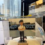 CUTEFIGUREHK 客製化男性警察人像公仔，生動還原了身穿白色短袖制服、深色長褲、黑色軍靴及配戴貝雷帽的警員造型，並擺出充滿自信的雙手交叉胸前姿勢。公仔背後配有 PTU 警察機動部隊的戶外大合照背景。底座設有專屬木紋牌匾，印有「量咩 Happy Retirement 2025 PTU Z1/E3 (2010-11) 仝人敬贈」的祝福語。這是一份極具心思的紀律部隊散水或榮休紀念禮物。