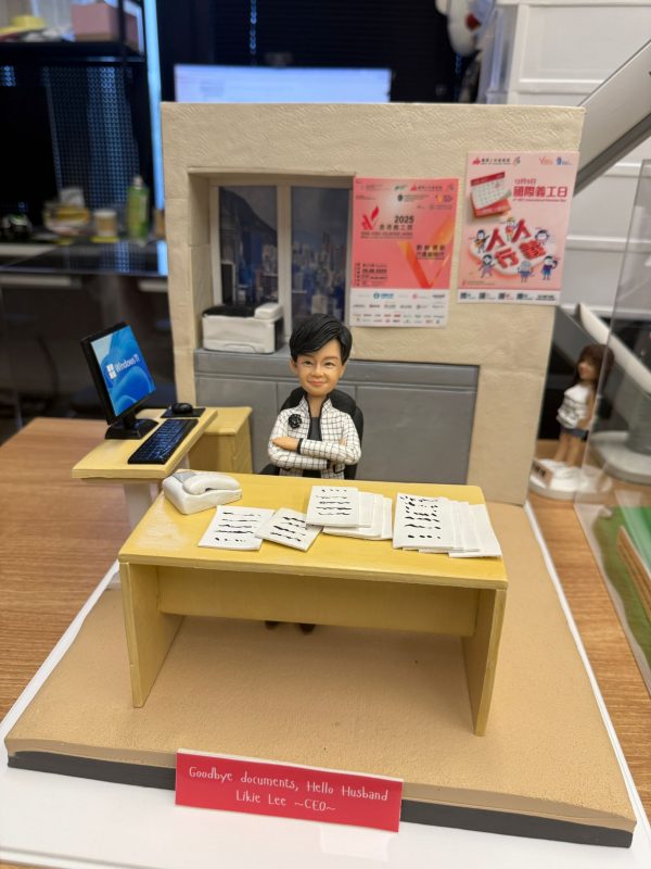 CUTEFIGUREHK 客製化退休禮物公仔。一個精緻的辦公室場景立體模型，主角是一位短髮女士，身穿黑白格紋外套，雙手交叉自信地坐在辦公桌前。黃色的辦公桌上放滿了文件和一部白色電話。旁邊的側桌有一部顯示 Windows 11 畫面的電腦屏幕及鍵盤滑鼠。背景牆上有窗戶透出城市高樓景色，窗台放有打印機，牆上貼有「2025 香港義工獎」及「國際義工日」的縮微海報。模型前方底座有一塊紅色名牌，用白字寫著「Goodbye documents, Hello Husband」及「Likie Lee CEO」。