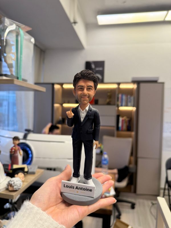 CUTEFIGUREHK 客製化男士公仔。人偶穿著深色西裝外套配白襯衫與白球鞋，展現商務休閒風格。右手舉起食指，面帶自信微笑。灰色圓形底座上帶有「Louis Antoine」專屬名牌及小金星圖案，是完美的升職或職場紀念禮物。