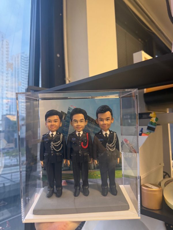 CUTEFIGUREHK 客製化三人紀律部隊人像公仔，三位男主角身穿整齊警察制服並佩戴精緻飾繩，背後配以總部大樓背景，並裝在透明亞加力展示盒中，是專為同袍升職、調職或退休訂製的專屬紀念禮物。