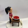 圓形白色底座上的客製公仔：紮馬尾、穿紫紅色上衣的角色站在深木色小桌後方，桌上白盤盛裝滿滿紅色辣椒；前方放置寫有「Thank You」字樣的小牌。背景以白紙遮擋，多為室內環境。