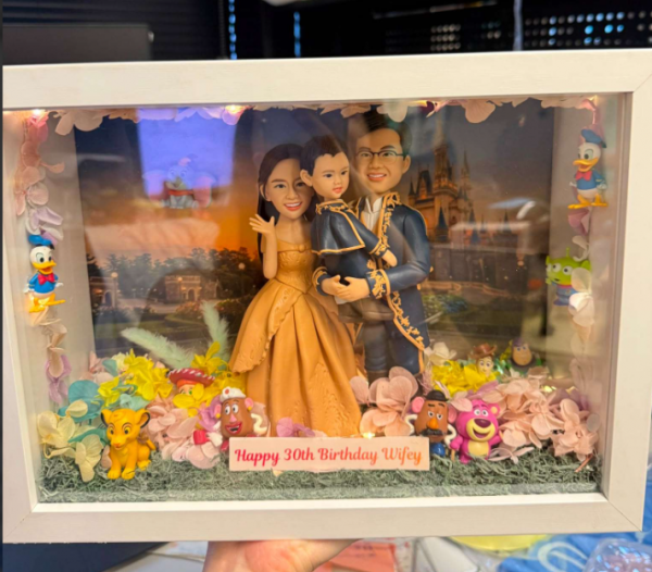 白色相框展示盒中的場景公仔：一對穿晚禮服的成人與一名幼童站在中央，背景是夕陽下的城堡畫面；腳邊鋪有草地與粉彩花瓣，四周擺放多個卡通風小擺件；底部銘牌寫有「Happy 30th Birthday Wifey」。