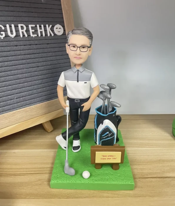 為一位熱愛高爾夫球的男士訂製的人像公仔榮休禮物。他身穿高爾夫球服飾，自信地站在果嶺上，旁邊有高爾夫球袋，前方的牌子寫著「Best wishes! Enjoy your life」。