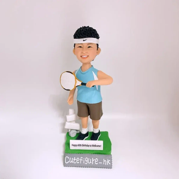 送給Welcome的60歲生日禮物人像公仔。他身穿網球服，笑容燦爛，旁邊有一疊廁紙作為幽默的點綴。名牌上寫有生日快樂的祝福。