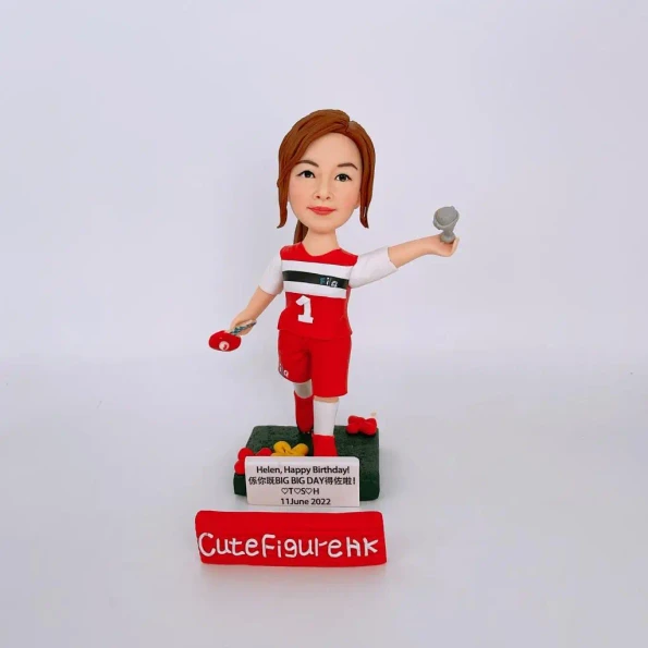 送給Helen的生日禮物人像公仔。她身穿1號紅色乒乓球衣，一手拿球拍，一手拿著麥克風，底座上有名牌寫著生日祝福。