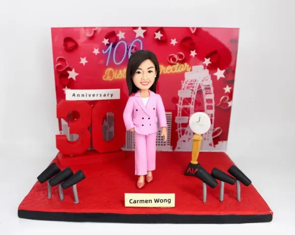 一張為慶祝上司榮升及公司週年慶而訂製的人像公仔照片。圖中是主角Carmen Wong的人像公仔，她身穿粉紅色套裝，自信地站在一個佈滿咪高峰和獎座的頒獎典禮舞台上，背景有30週年紀念標誌。這款人像公仔是慶祝公司上市、祝賀開張禮物的理想選擇。