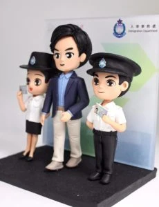 入境處公仔禮物 榮休禮物 有覺得很熟面口嗎？ 感謝入鏡事務處的信任。圖中是呼籲市民換身分證的廣告，相信不少人都見過呢！中間卡通人像是15cm的張先生，而旁邊則是兩隻12cm的卡通人像，他們是穿著制服的入鏡事務處職員，手上還拿著香港身分證作呼籲呢！而背景則是2D平面設計的入鏡事務處背景