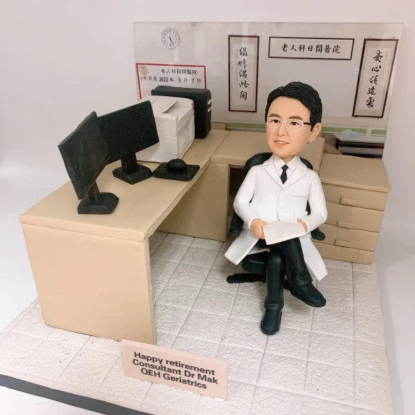一張展示醫生退休禮物的照片，圖中是一個為伊利沙伯醫院(QEH)老人科麥醫生訂製的醫生公仔。這份感謝醫生禮物重現了他的辦公室，背景有『醫心濟世人』等書法字畫，是個極具心思的醫生禮物