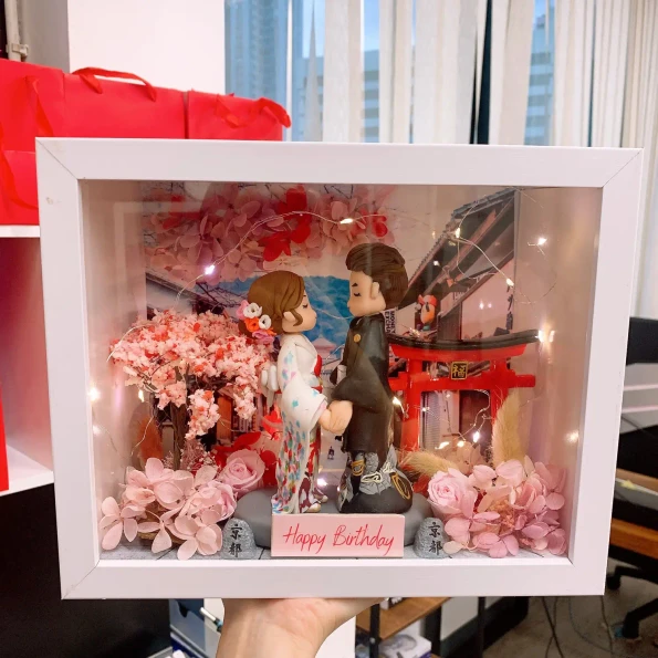 白色相框內的日系情侶場景：女生穿白底彩點和服配花髮飾，男生穿深色和服，兩人面對面牽手站立。背景有紅色鳥居、日式街景與櫻花樹，前景點綴粉色花材與小石碑，上方繞有暖光燈串，底牌寫著「Happy Birthday」。