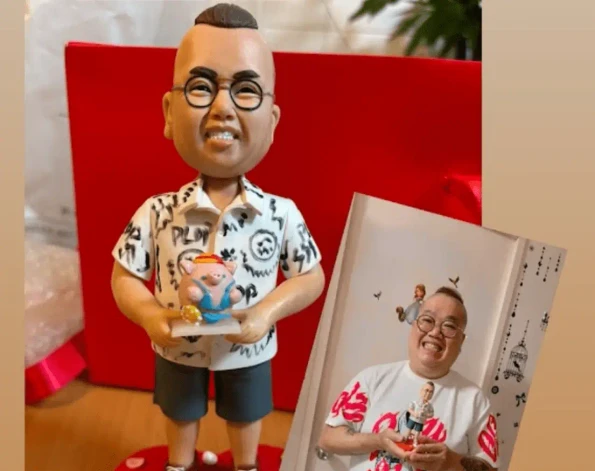 一張展示客製化生日大壽禮物人像公仔的客戶分享圖。主圖是一個根據真人製作的Q版公仔，公仔手捧小豬撲滿，站在心形草莓底座上。右下角附有真人原型開心拿著自己公仔的對比照，圖片上方有「好正好靚好得意」的文字讚美。這個也可以作為退休禮物也不錯