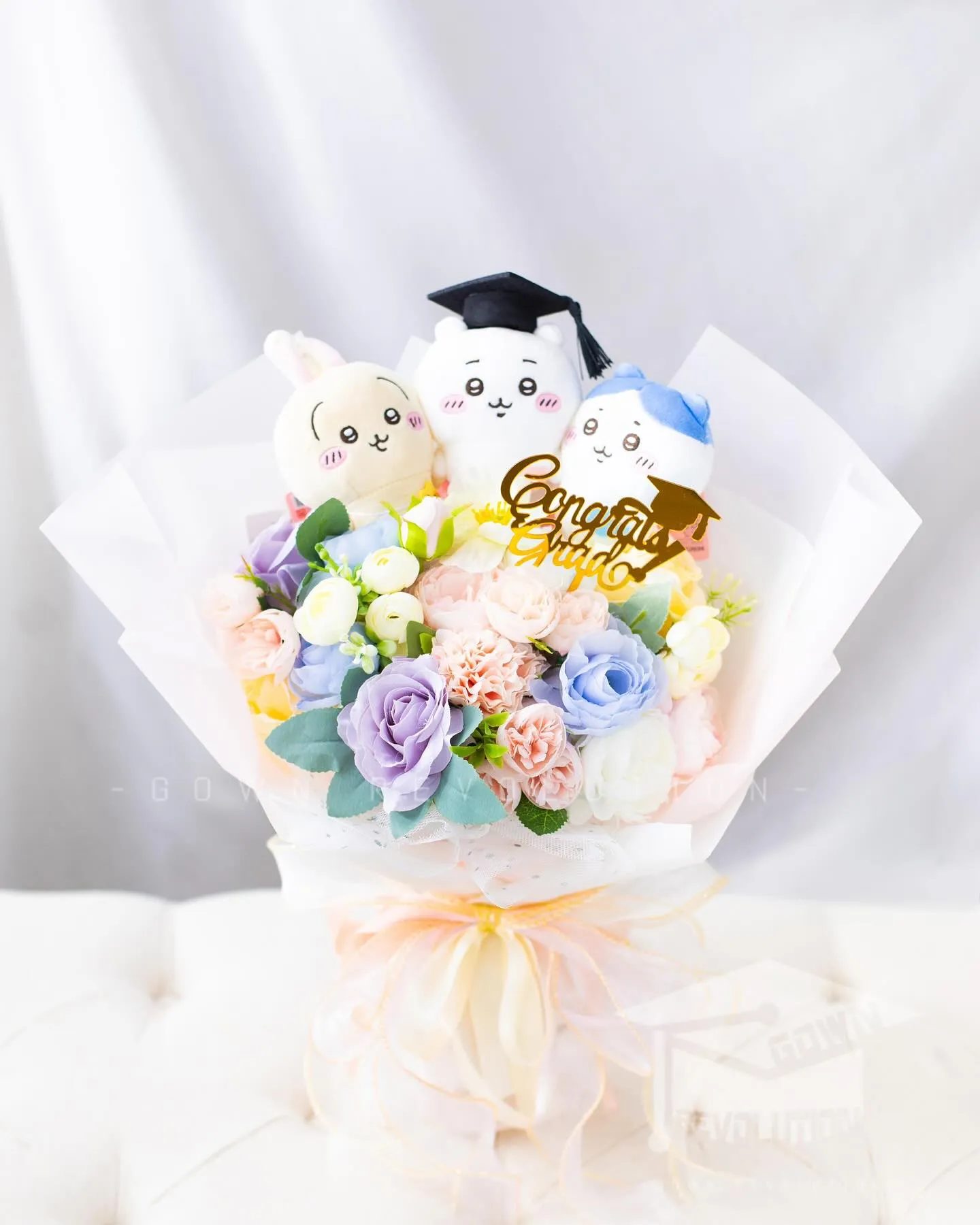 一束色彩繽紛的公仔花束，包含三隻可愛的卡通毛絨公仔，其中一隻戴著畢業帽，花束上插有「Congrats Grads」字樣，是慶祝畢業或生日的禮物推介。