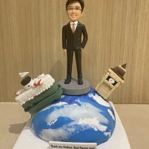 一位男性人像公仔穿著西裝，站在地球造型底座上，周圍有英國大笨鐘和遊輪裝飾