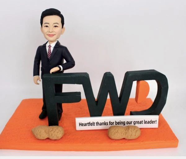 一款為FWD富衛保險的卓越領導者訂製的退休禮物人像公仔。公仔身穿西裝，自信地靠在巨大的FWD公司標誌上，橙色的底座上有一塊寫著「衷心感謝您成為我們偉大的領導者」的銘牌和兩顆象徵祝福的花生，是一份充滿敬意與巧思的禮物。