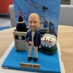 一個穿著藍色外套和米色褲子的人像公仔站在立體場景中，背景有櫻花、電線杆和輪船元素，旁邊有時鐘塔和感謝字牌，色彩鮮明。