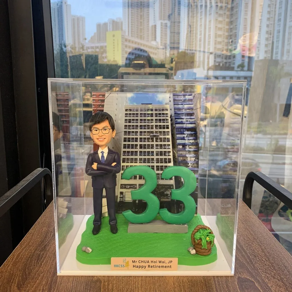 香港社會服務聯會（HKCSS）總裁蔡海偉先生，JP的人像公仔，他身穿西裝、雙臂交叉，身旁有一個巨大的綠色數字「33」，象徵他33年的服務年資。這是一款為他精心訂製的榮休禮物。