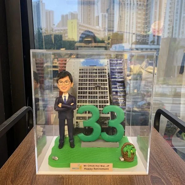 香港社會服務聯會（HKCSS）總裁蔡海偉先生，JP的人像公仔，他身穿西裝、雙臂交叉，身旁有一個巨大的綠色數字「33」，象徵他33年的服務年資。這是一款為他精心訂製的榮休禮物。