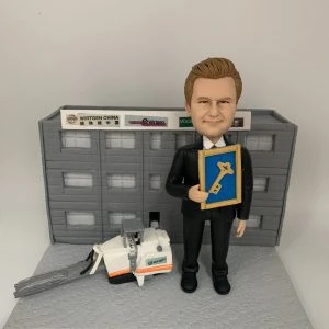 男士人像公仔身穿西裝,手持獎狀,站在立體建築背景前,旁邊配有立體工程車模型。背景建築牆上有公司標誌,整體設計突出立體背景、立體建築和工程車元素。這款人像公仔適合作為升職禮物、上司禮物或公司禮物。