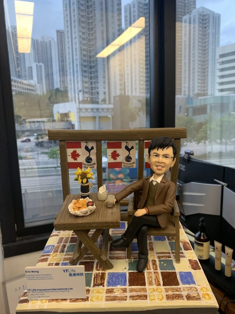 男士人像公仔身穿啡色西裝，坐在立體酒吧造型的桌椅旁，桌上有食物、啤酒和裝飾品，背景牆掛有酒吧裝飾旗幟。場景設計突出立體背景和酒吧元素。這款人像公仔適合作為升職禮物、上司禮物或公司禮物。